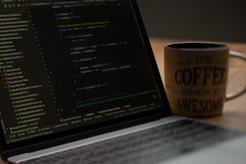 A silver laptop with a black keyboard sitting on a wooden table, displaying lines of code in a text editor on its bright screen. The background features a cozy indoor setting with soft lighting, blurr
